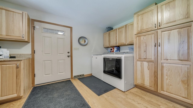 clothes washing area featuring light wood-style flooring, independent washer and dryer, and cabinet space