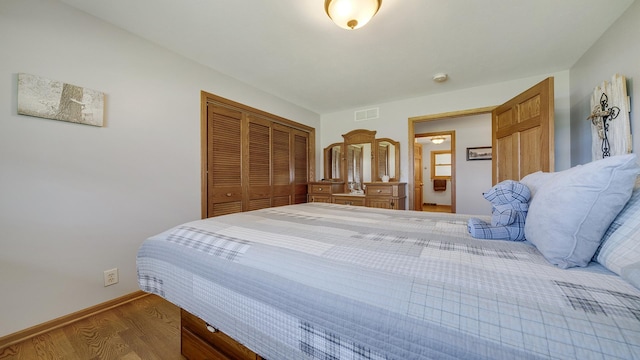bedroom with baseboards, wood finished floors, visible vents, and a closet