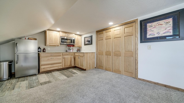 kitchen featuring light brown cabinets, light wood finished floors, light countertops, light colored carpet, and appliances with stainless steel finishes
