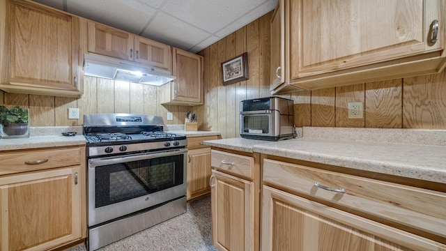 kitchen with light brown cabinetry, a drop ceiling, light countertops, under cabinet range hood, and gas stove