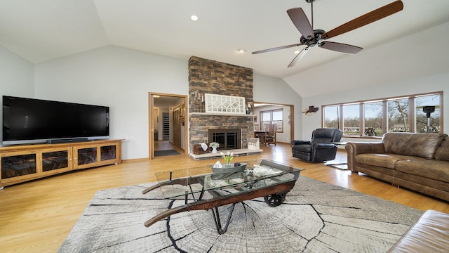 living area featuring a stone fireplace, wood finished floors, baseboards, high vaulted ceiling, and ceiling fan