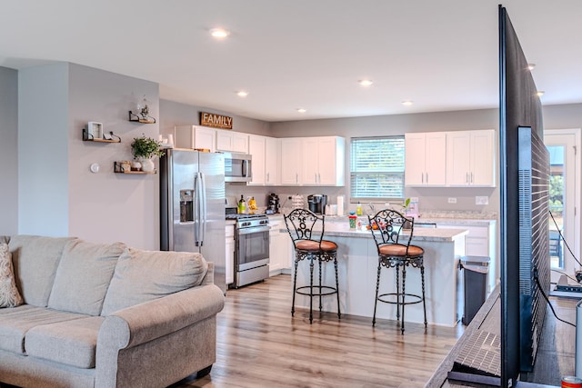 kitchen with open floor plan, a breakfast bar area, stainless steel appliances, light countertops, and white cabinets