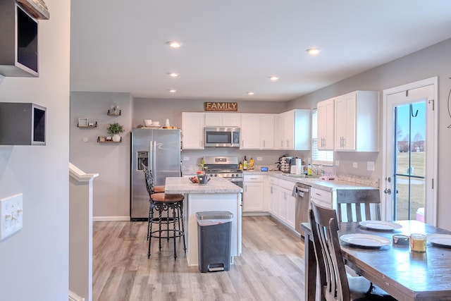 kitchen with stainless steel appliances, a center island, a sink, light wood-style floors, and white cabinetry