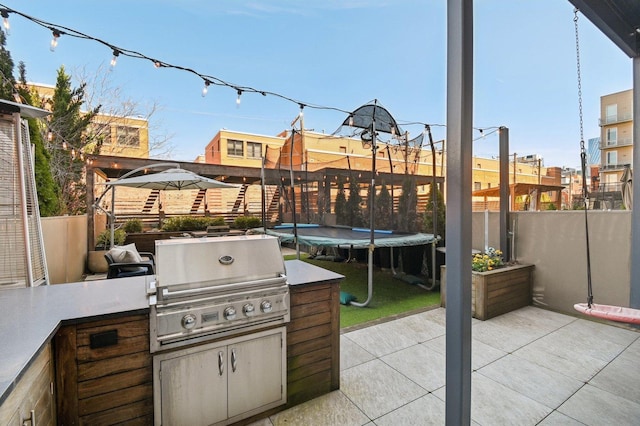 view of patio featuring fence, exterior kitchen, a trampoline, and grilling area