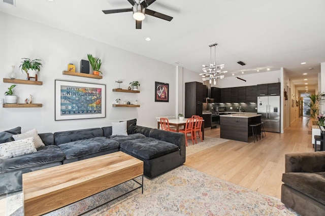living area with light wood-type flooring, recessed lighting, ceiling fan with notable chandelier, and visible vents