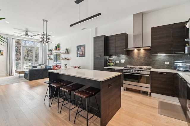kitchen with gas stove, a breakfast bar area, light countertops, wall chimney exhaust hood, and a center island