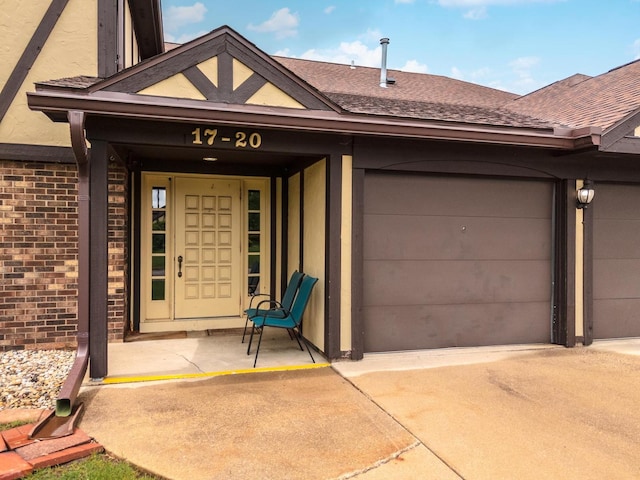view of exterior entry with roof with shingles, a garage, driveway, and brick siding