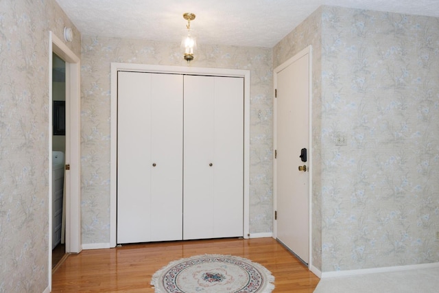 foyer entrance with baseboards, wallpapered walls, and wood finished floors