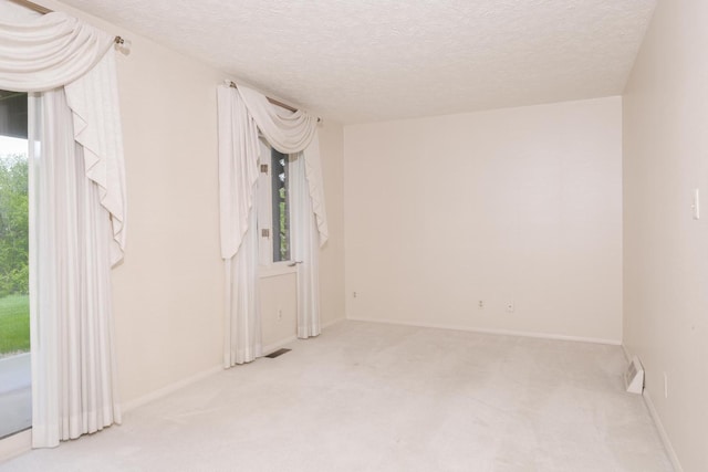 unfurnished room with a textured ceiling, visible vents, baseboards, and carpet