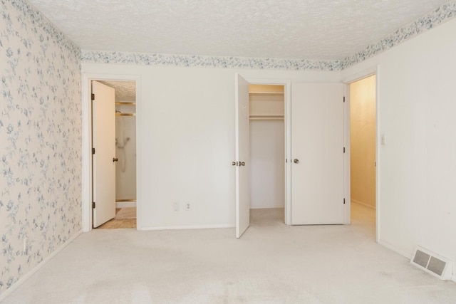 unfurnished bedroom featuring visible vents, a textured ceiling, carpet floors, and wallpapered walls