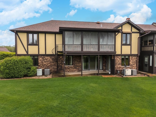 back of property with central air condition unit, brick siding, a lawn, and stucco siding