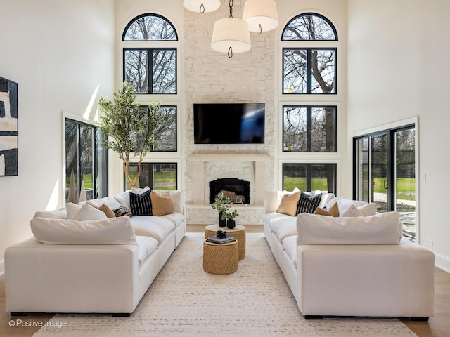 living room with plenty of natural light, wood finished floors, a towering ceiling, and a fireplace