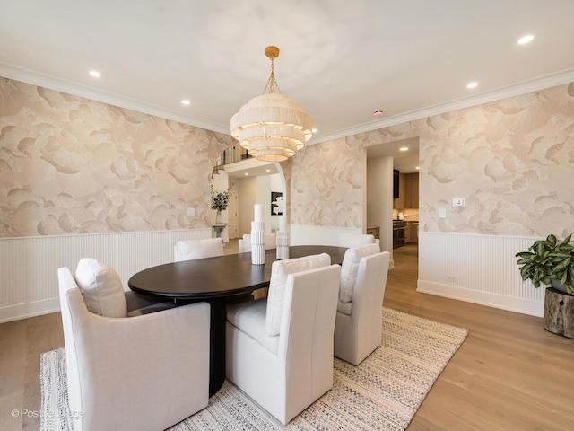 dining area featuring wallpapered walls, an inviting chandelier, light wood-type flooring, crown molding, and wainscoting