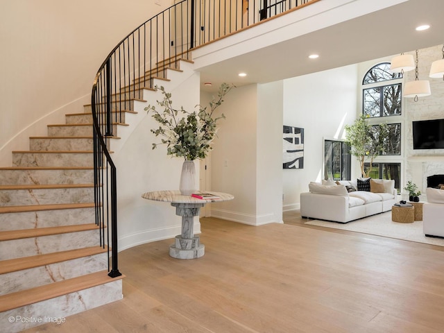 stairway with recessed lighting, a high ceiling, wood finished floors, baseboards, and a large fireplace