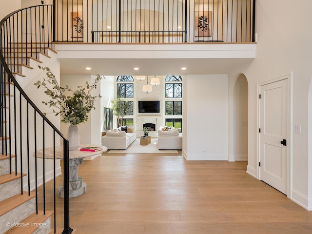 entrance foyer featuring baseboards, wood finished floors, a high ceiling, and a large fireplace