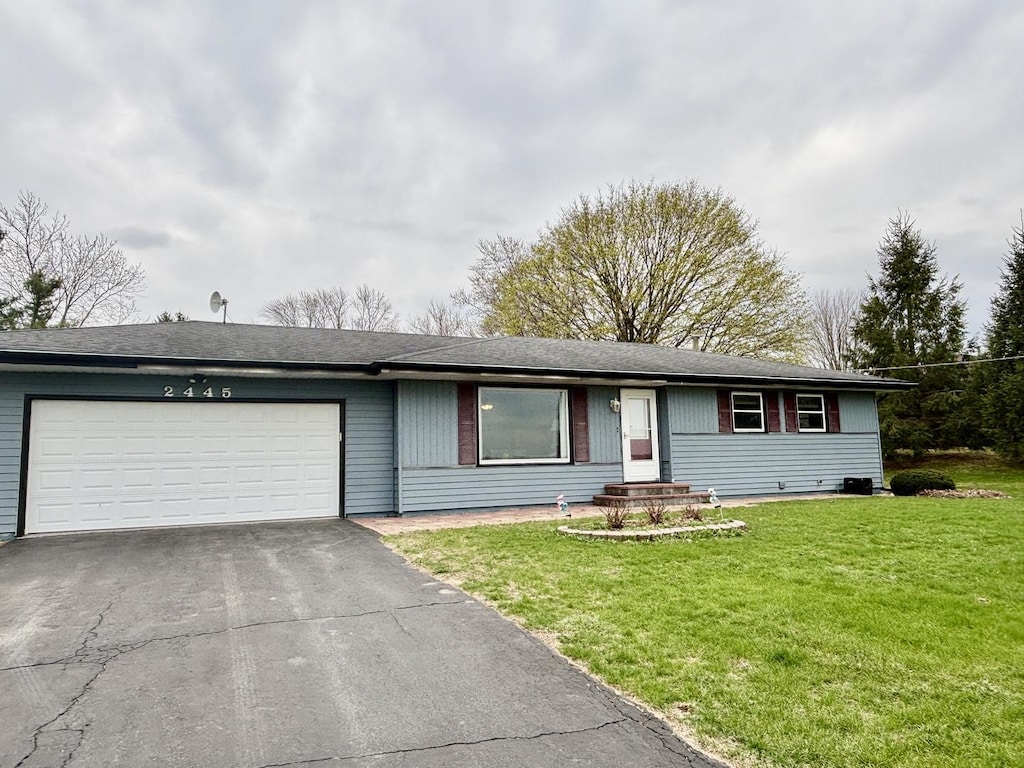 ranch-style home with an attached garage, a front lawn, and aphalt driveway