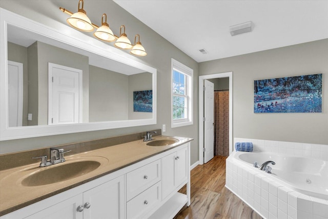 full bathroom featuring a sink, double vanity, a jetted tub, and wood finished floors