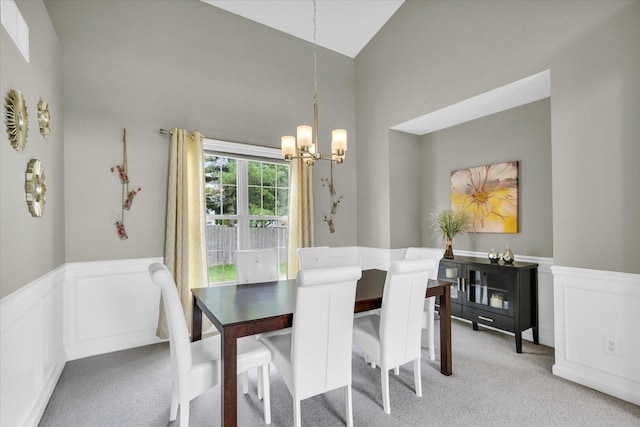 dining room with wainscoting, lofted ceiling, a decorative wall, light carpet, and a chandelier