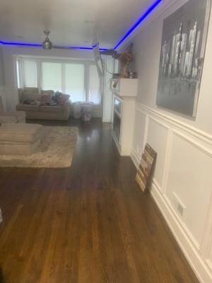 living area featuring wainscoting, a fireplace, a decorative wall, and dark wood-style flooring