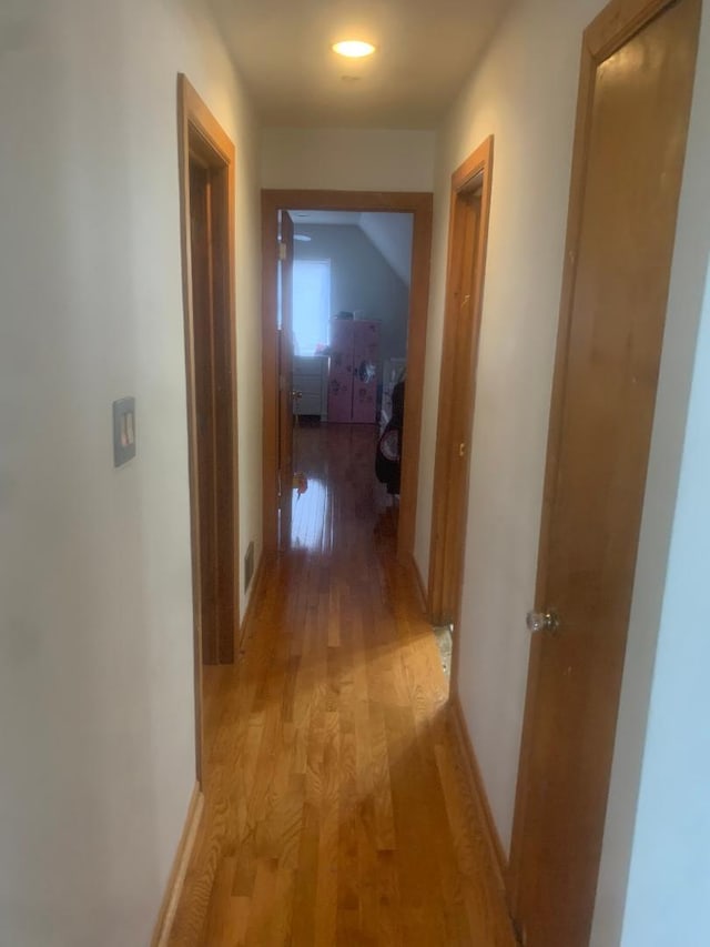 hall featuring baseboards, light wood-style flooring, and visible vents