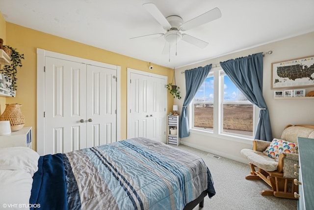 carpeted bedroom featuring ceiling fan, baseboards, visible vents, and two closets