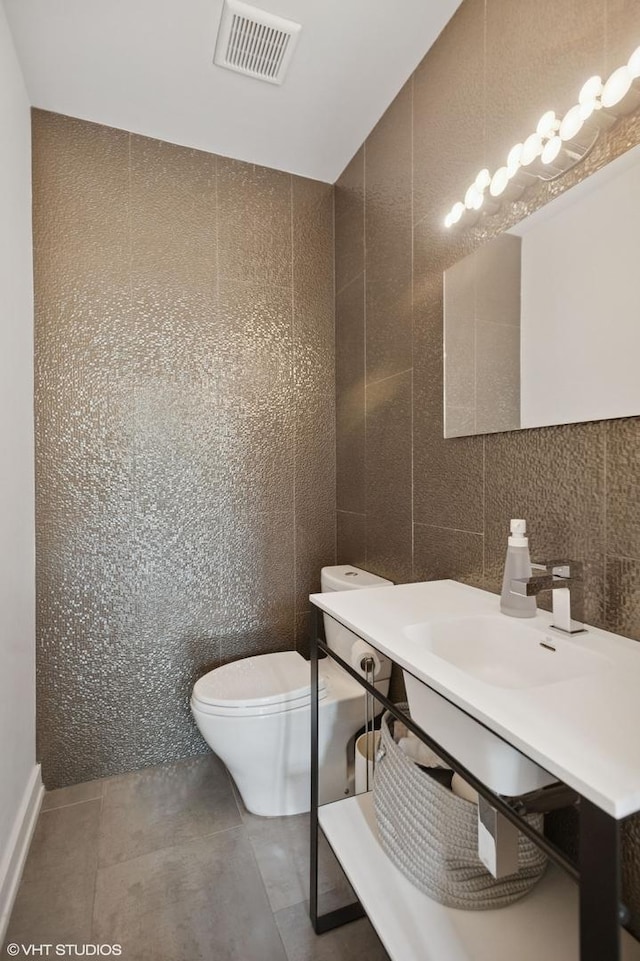 half bathroom with tile walls, toilet, visible vents, a sink, and tile patterned flooring