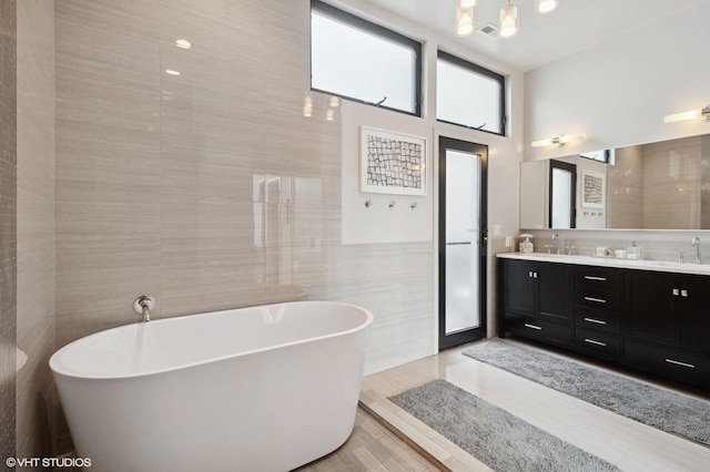 full bathroom with tile walls, a sink, a freestanding bath, double vanity, and wood finished floors
