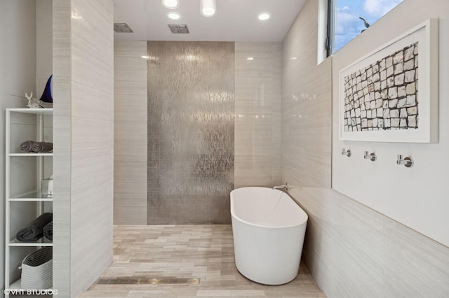 full bath with tile walls, visible vents, a freestanding bath, and recessed lighting