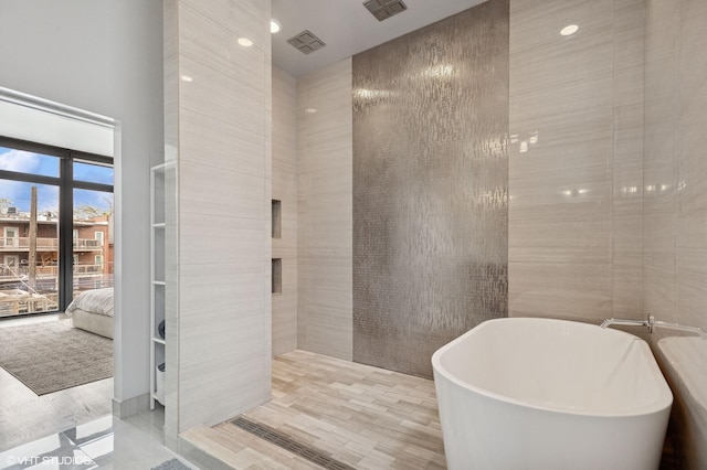 bathroom featuring a soaking tub, connected bathroom, visible vents, and tile walls