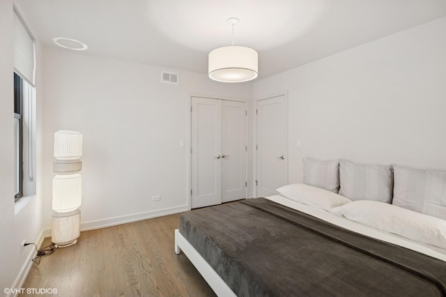 bedroom with baseboards, a closet, visible vents, and wood finished floors