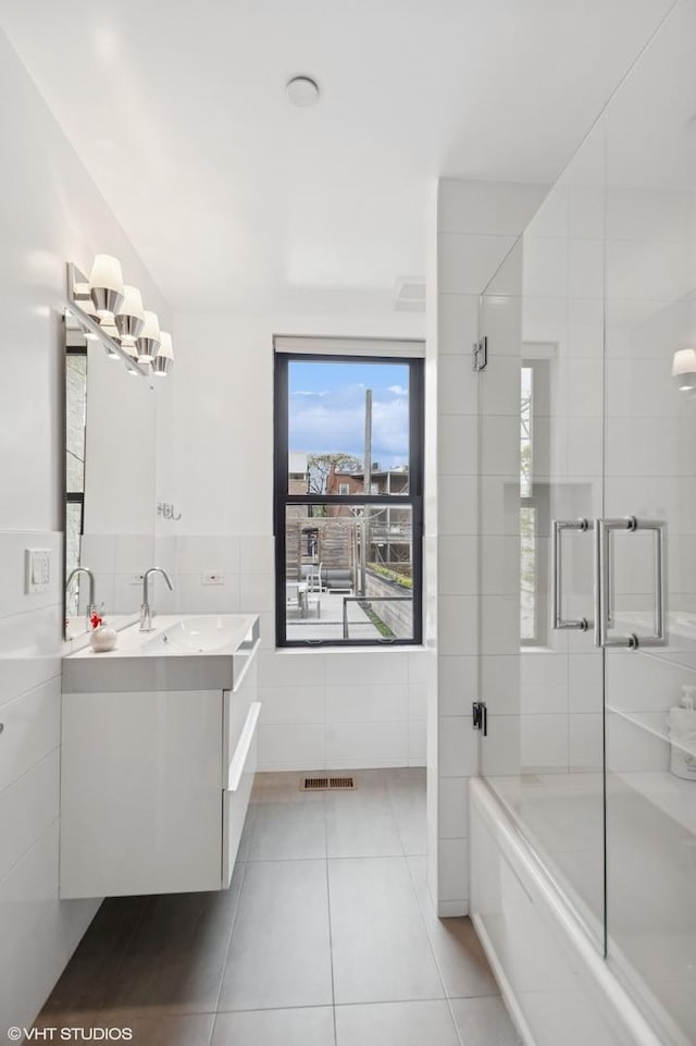 bathroom featuring a shower with shower door, tile walls, vanity, visible vents, and tile patterned flooring