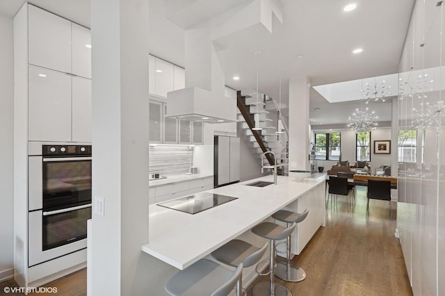 kitchen with modern cabinets, a sink, black electric stovetop, double oven, and white cabinets