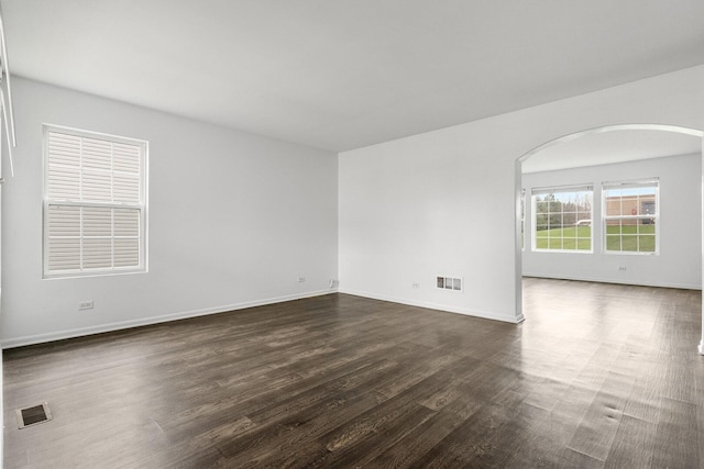 169 Waterbury Cir, Oswego, IL 60543 - spare room featuring dark wood finished floors, arched walkways, visible vents, and baseboards