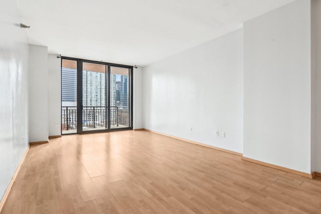 empty room featuring a wall of windows, baseboards, and light wood finished floors
