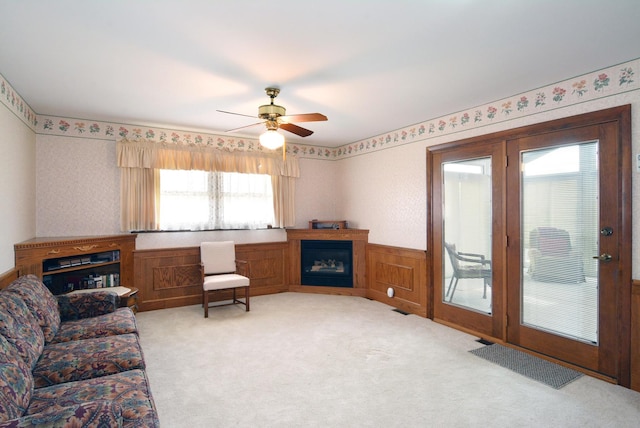 living area with light colored carpet, ceiling fan, a glass covered fireplace, and a wainscoted wall