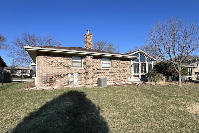 back of property featuring a chimney, brick siding, a yard, and central AC unit