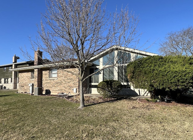 view of side of property featuring a chimney, brick siding, a yard, and cooling unit