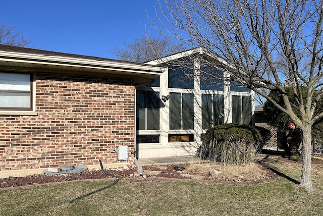 view of property exterior featuring a lawn, a sunroom, and brick siding