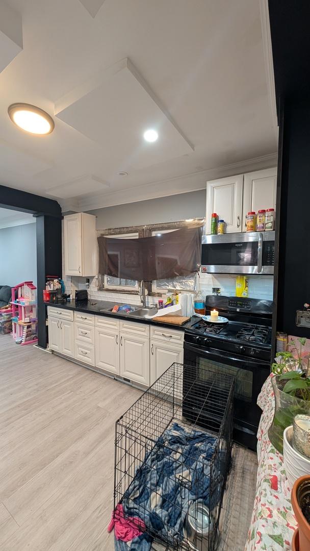 3039 W Flournoy St, Chicago, IL 60612 - kitchen featuring white cabinets, a sink, stainless steel microwave, light wood-style flooring, and black gas range