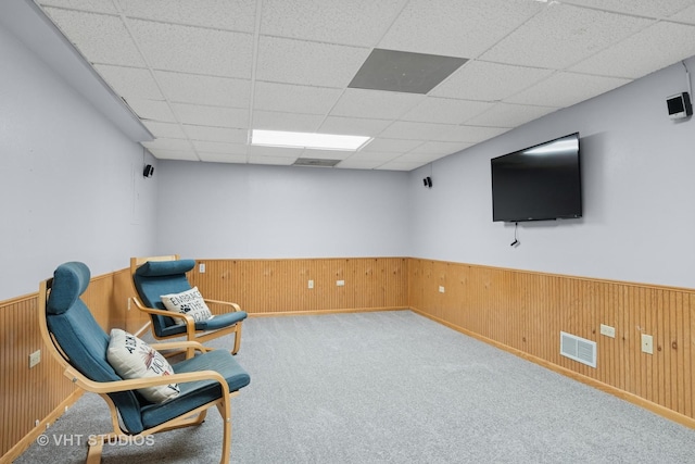 living area featuring visible vents, wood walls, wainscoting, and a drop ceiling