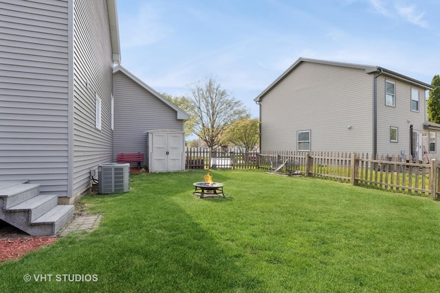 view of yard featuring an outdoor structure, a fire pit, a fenced backyard, central air condition unit, and a storage shed