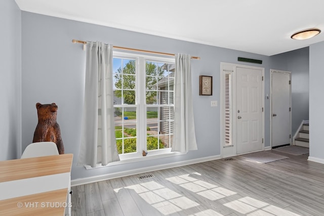 foyer entrance with baseboards, stairs, wood finished floors, and visible vents