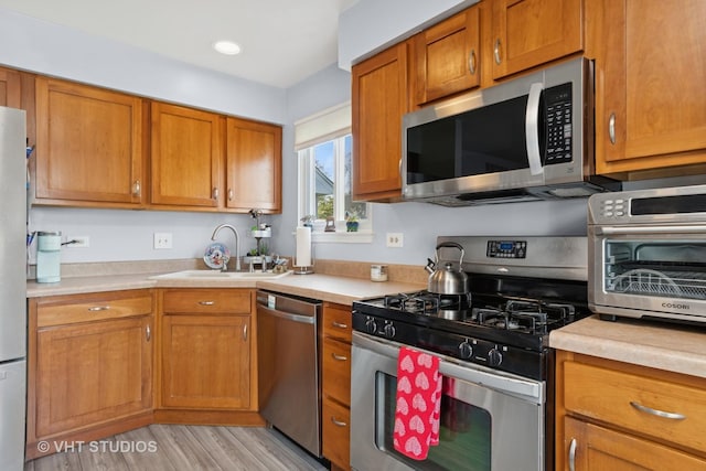 kitchen with light countertops, stainless steel appliances, brown cabinetry, and a sink