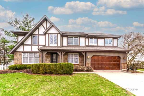 english style home featuring brick siding, driveway, a front yard, and a garage