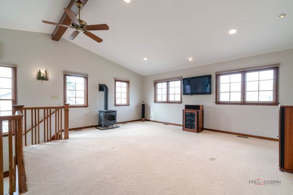 unfurnished living room featuring a ceiling fan, vaulted ceiling with beams, light carpet, a wood stove, and baseboards