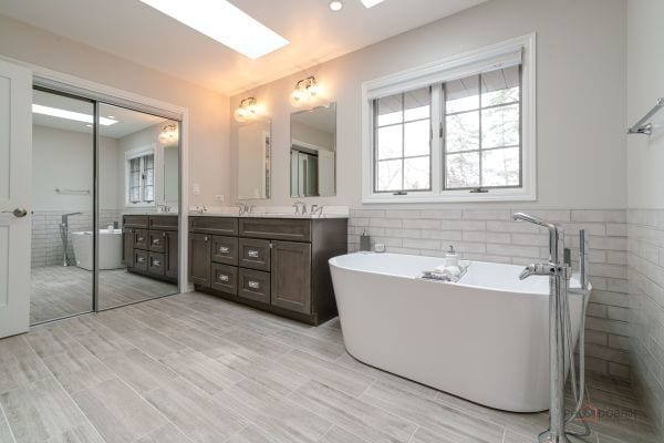 full bathroom featuring a wainscoted wall, tile walls, a skylight, a freestanding tub, and vanity
