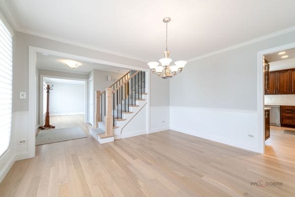 unfurnished dining area featuring stairway, light wood finished floors, ornamental molding, and an inviting chandelier