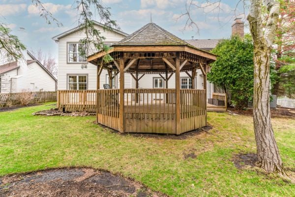 back of property featuring a gazebo, a chimney, fence, a lawn, and a deck