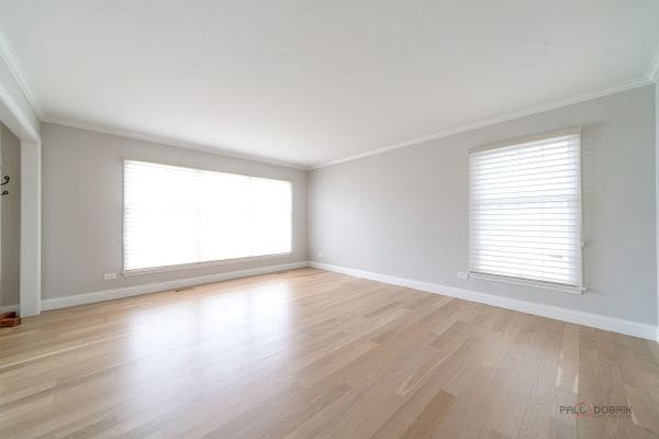 empty room featuring light wood-type flooring, baseboards, and ornamental molding