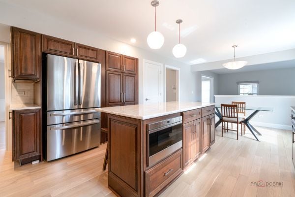 kitchen with a center island, light wood-style floors, pendant lighting, light countertops, and appliances with stainless steel finishes